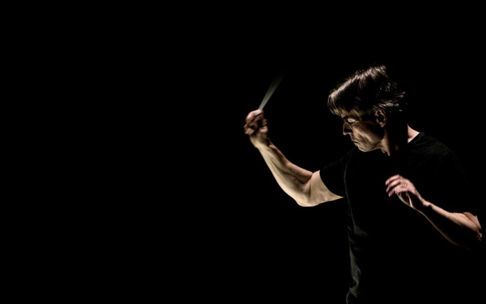 Conductor Esa-Pekka Salonen againt an all-black background, conducting