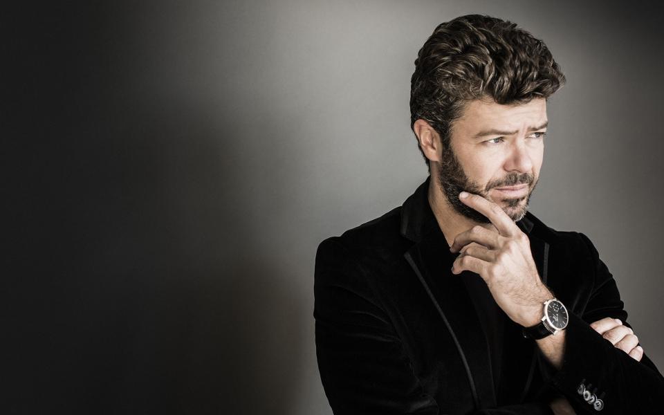 Conductor Pablo Heras-Casado wearing a black velvet blazer, holding his hand to his face, looking off camera