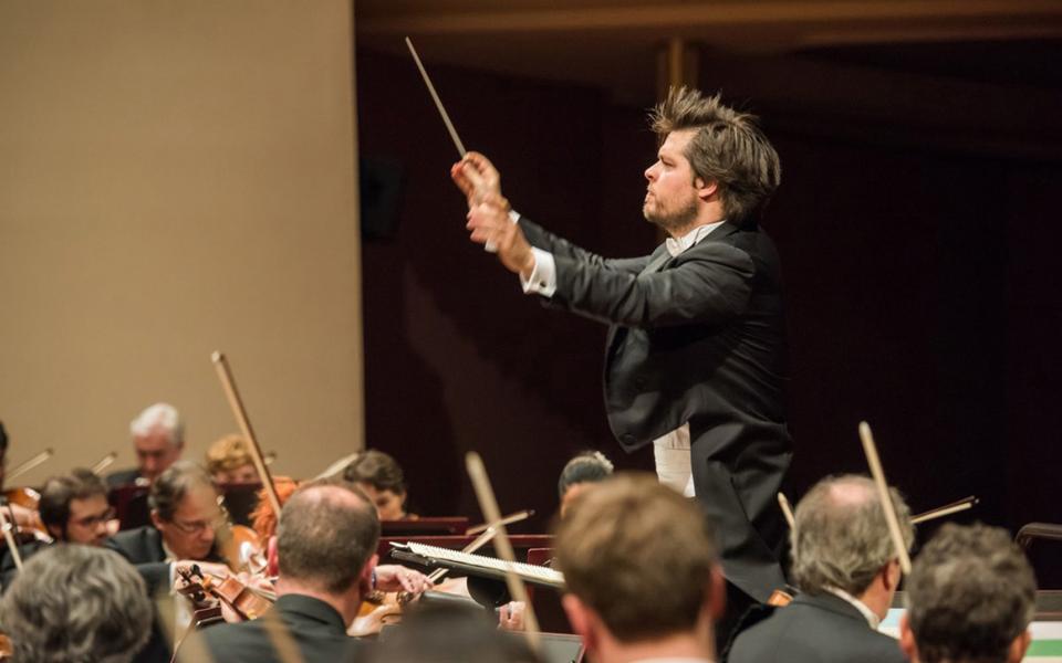 Conductor Juraj Valcuha, on stage during a concert, holding his baton, wearing tails