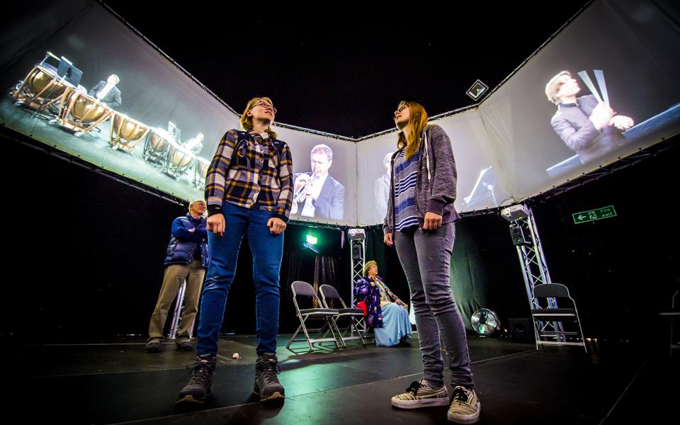 Two young women wearing sporty clothing listen to installation at The Virtual Orchestra