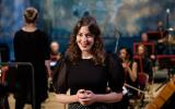 Photo of presenter Lucy Drever at the Philharmonia Sessions, smiling, Philharmonia Orchestra in the background