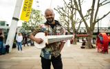 Soumik Datta standing on the Southbank with sarod looking into camera and smiling