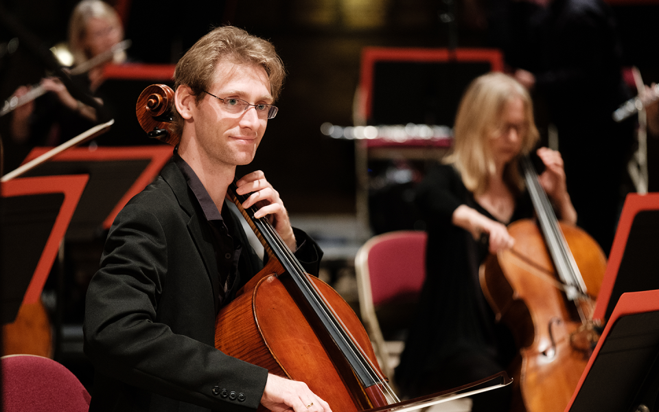 Richard Birchall, member of the Philharmonia, playing cello and smiling into the distance