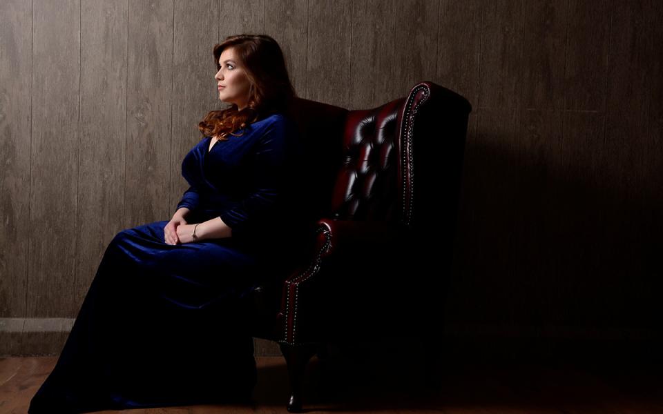 Rebecca Hardwick from the side. She is sitting in a dark leather chair against a dark wooden background