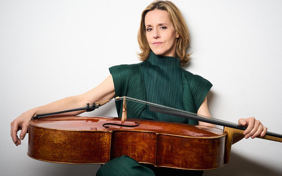 Sol Gabetta holds her cello across her lap on a white background
