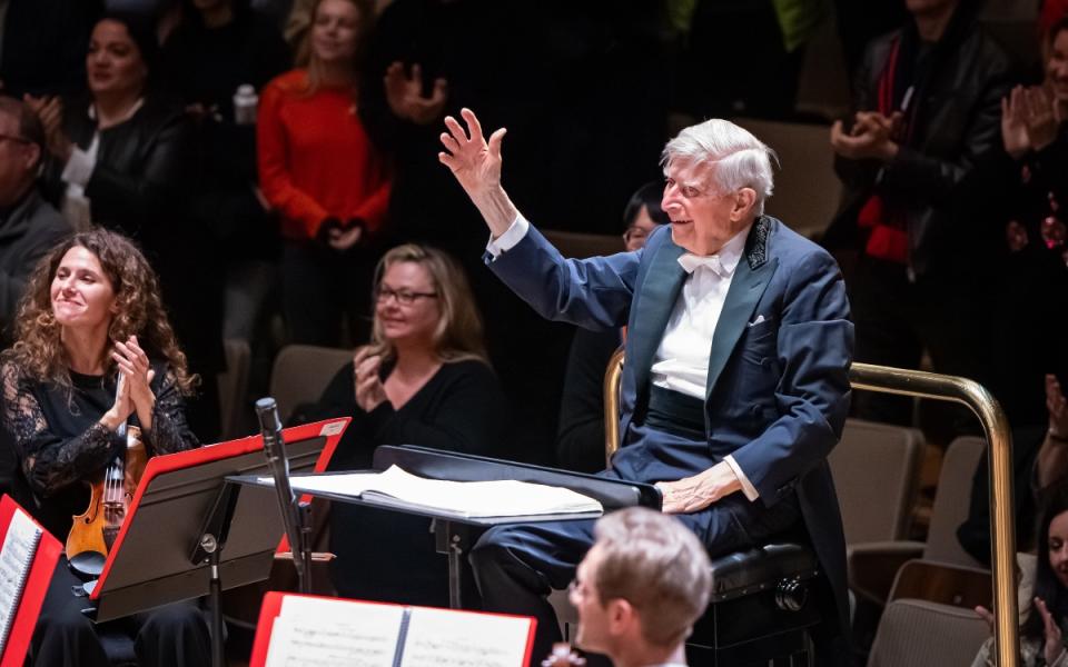 Herbert Blomstedt seated at the podium of the Philharmonia, similing with his right arm raised, receiving applause after conducting Mahler 9 in November 2024