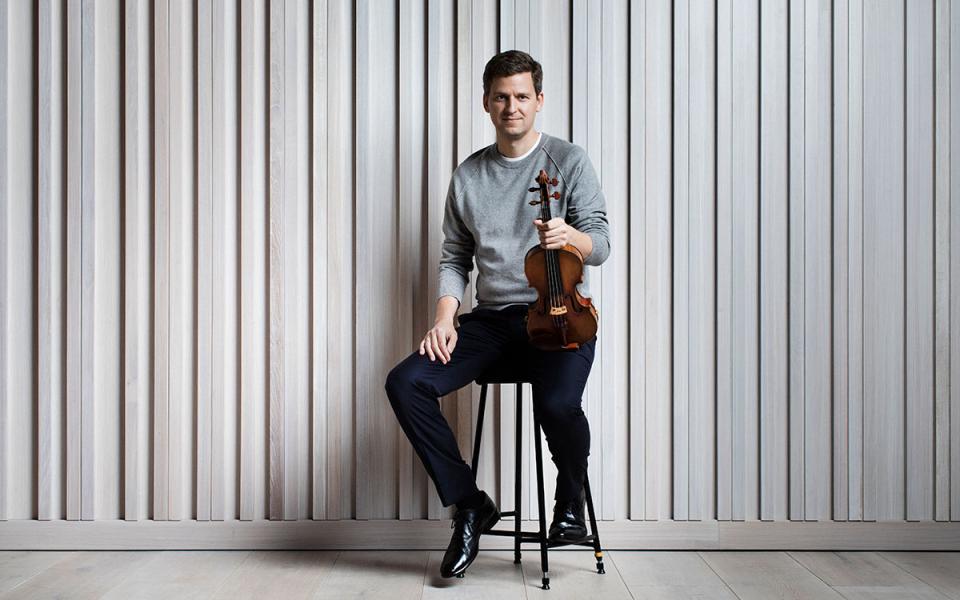James Ehnes, seated, holds his violin in front of a white background.