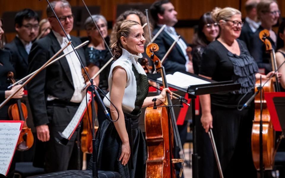 Sol Gabetta stands on stage with the Philharmonia Orchestra, facing the audience