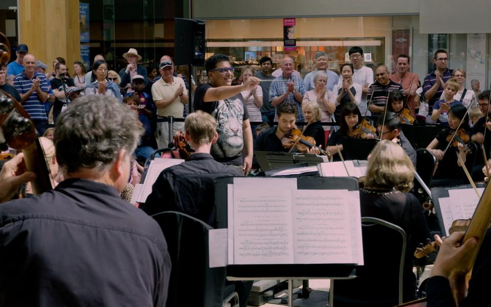Member of public conducting Philharmonia musicians at a pop up performance in a shopping centre