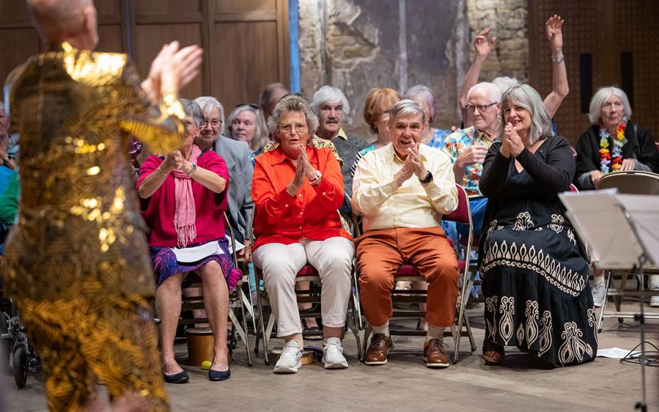 Adults sitting on chairs in rows, clapping their hands