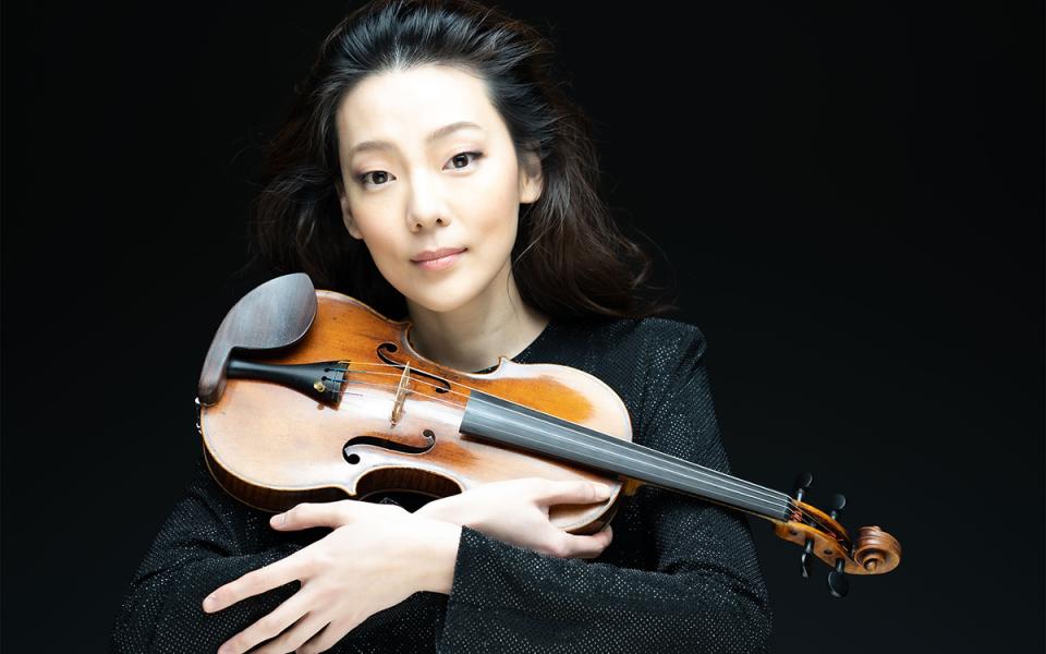 Clara-Jumi Kang against a black background holding her violin