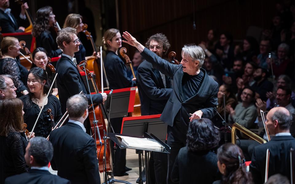 Esa-Pekka Salonen conducting standing amongst the orchestra with his arm outstretched