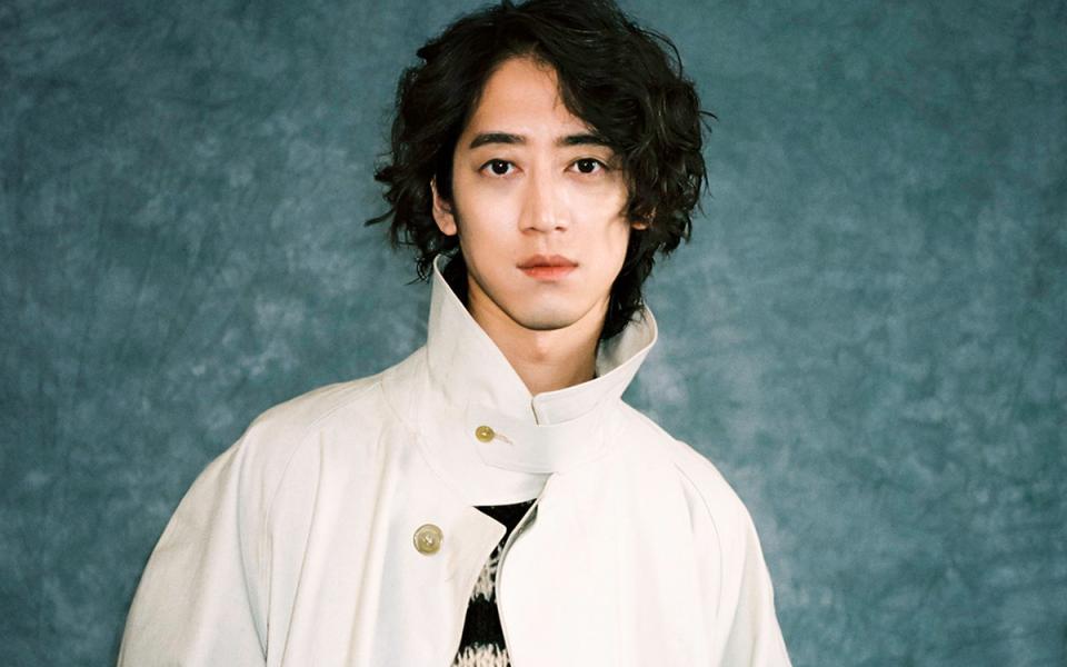 Hayato Sumino against a bluey green back ground in a ahite coat looking at the camera