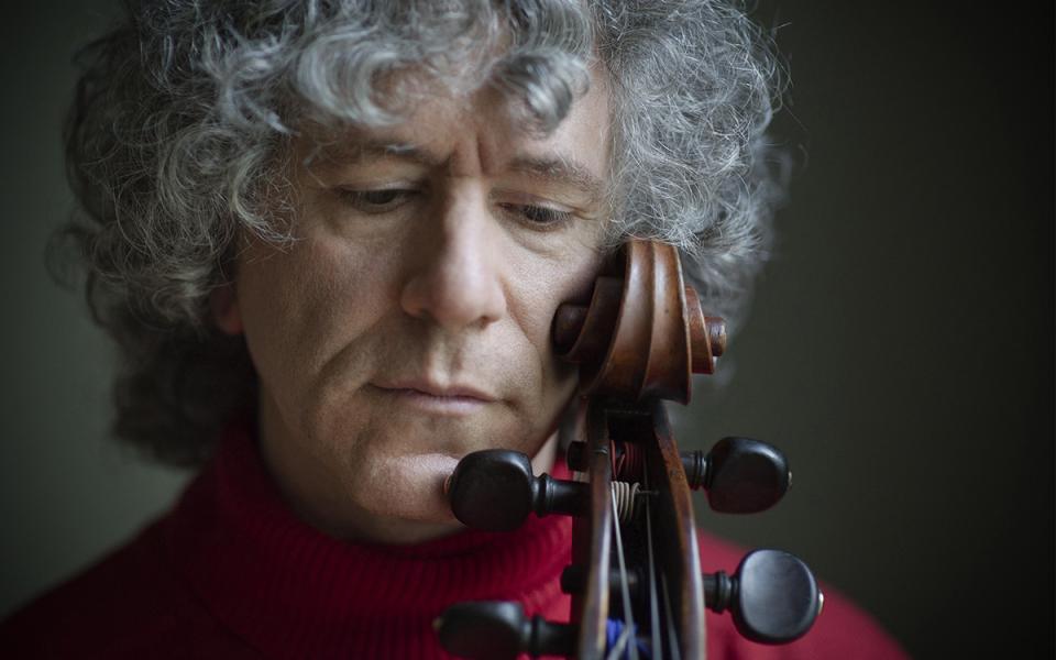 Steven Isserlis looking downwards with his head against the scroll of his cello.