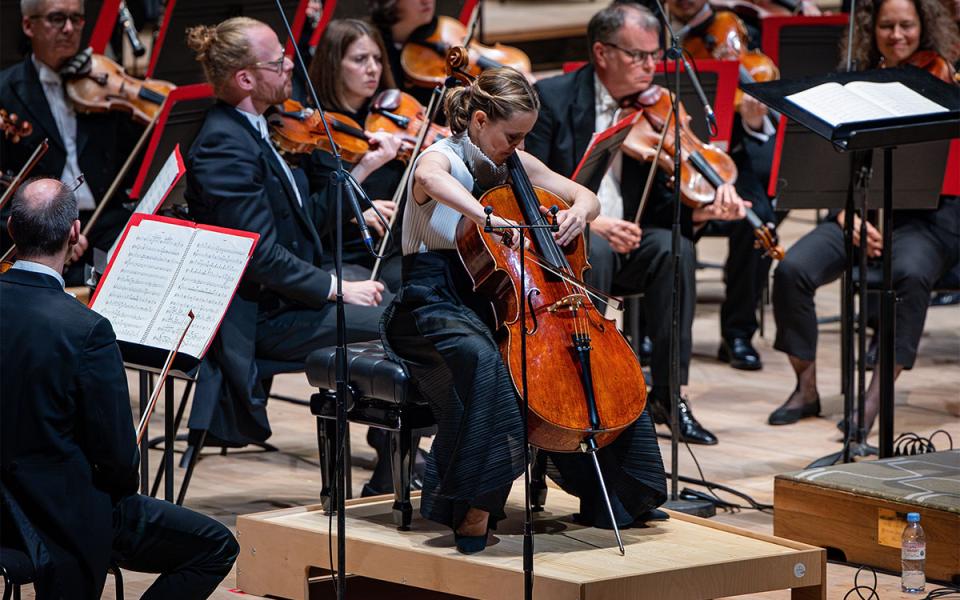 A close of shot of Sol Gabetta playing a concerto with the Philharmonia. Violinists are in the background.