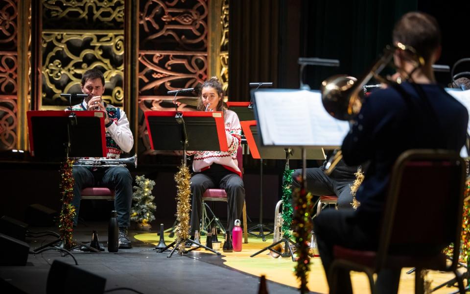 Brass musicians on stage at Soho Theatre Walthamstow, wearing Christmas jumpers with tinsel on their music stands