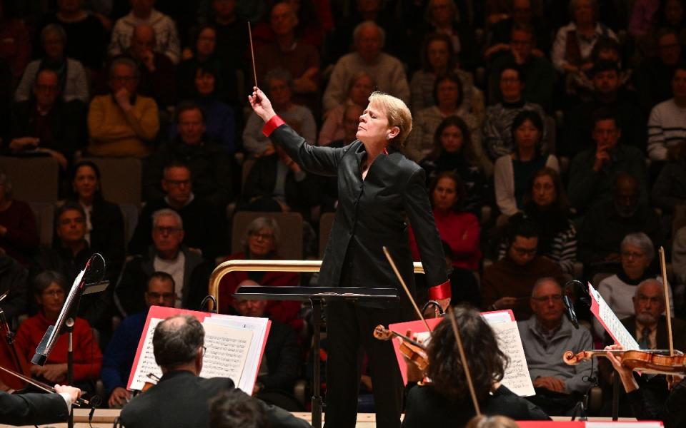 Marin Alsop stands in front of the Philharmonia orchestra, baton raised