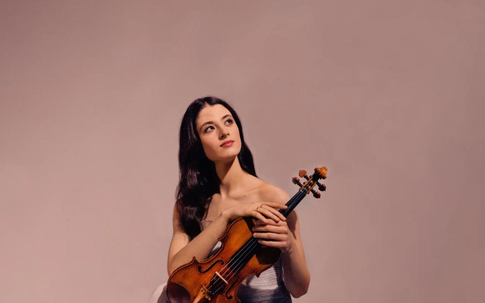 María Dueñas against a pastel pink background, holding her violin