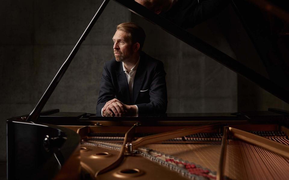 Leif Ove Andsnes leaning on a piano looking to the left